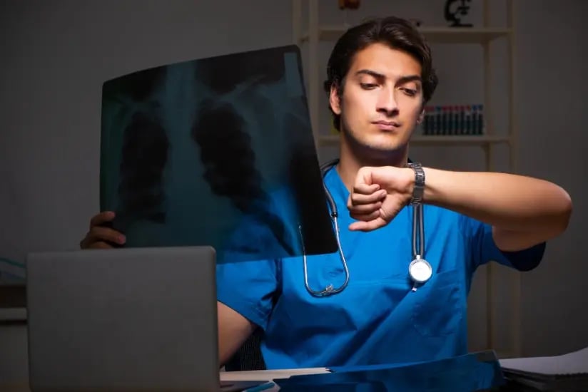 Männlicher Arzt in blauer Kleidung betrachtet ein Röntgenbild und schaut auf seine Uhr