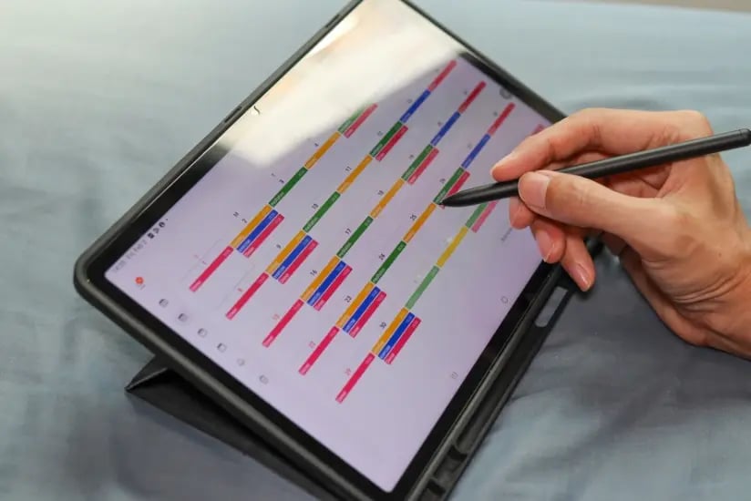 Hand benutzt einen Stift, um einen digitalen Kalender auf einem Tablet zu markieren